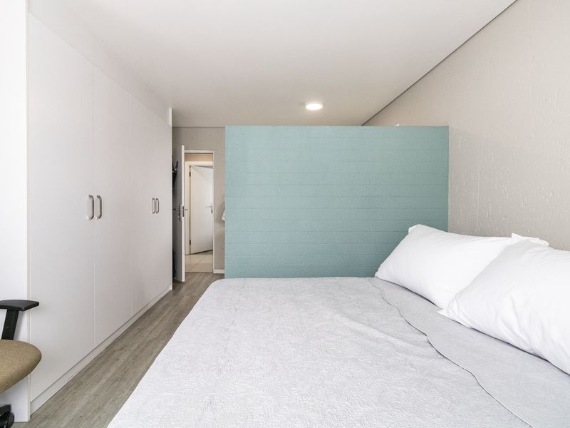 A modern bedroom featuring built-in white cupboards, laminate flooring, and a decorative blue partition wall creating a distinct sleeping area.