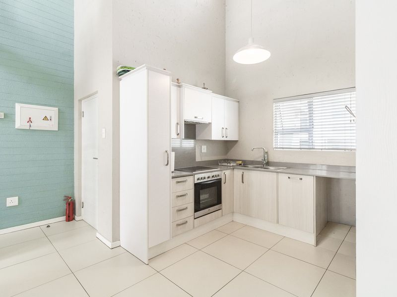 Compact modern kitchen featuring white cabinetry, integrated oven and hob, stainless steel sink, and neutral tiled flooring with high ceilings.
