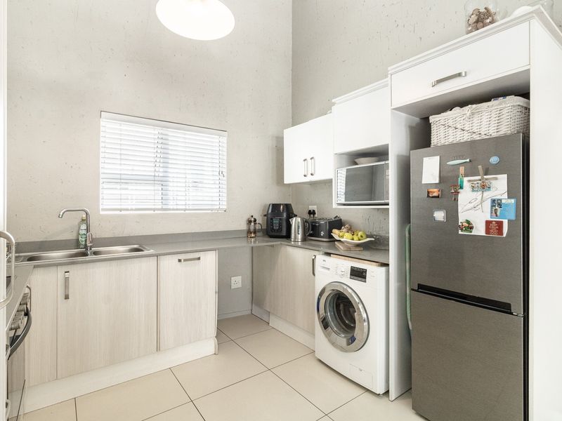 A functional kitchen featuring light wood-finish cabinetry, stone-look countertops, a double sink, and integrated appliance space with tiled flooring.