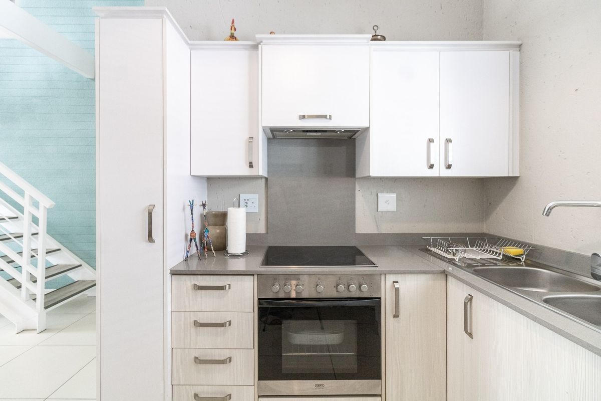 Compact modern kitchen featuring white cabinetry, stone countertops, integrated electric hob and oven, and a stainless steel sink.