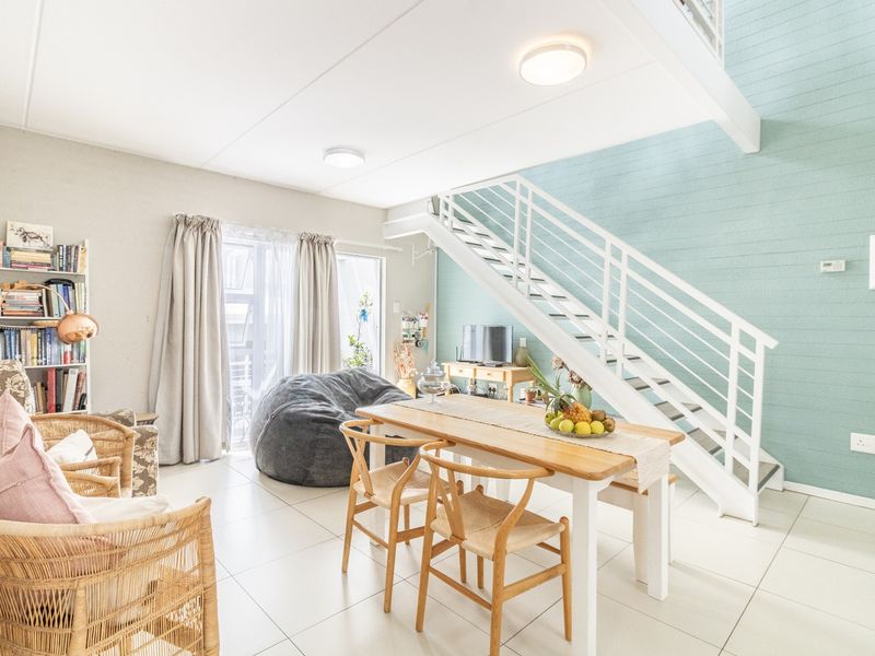 Bright open-plan living and dining area featuring a modern staircase, tiled flooring, and a light blue panelled feature wall.