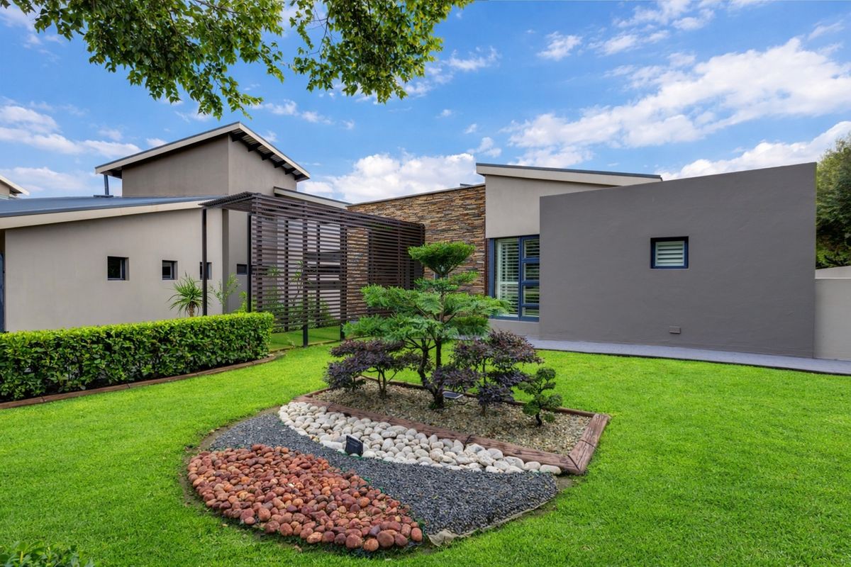 A well-maintained rear garden featuring a modern architectural design with stone cladding, a timber pergola, and manicured lawn.