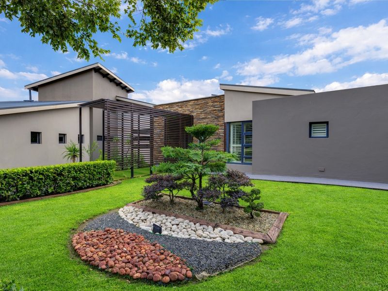 A well-maintained rear garden featuring a modern architectural design with stone cladding, a timber pergola, and manicured lawn.