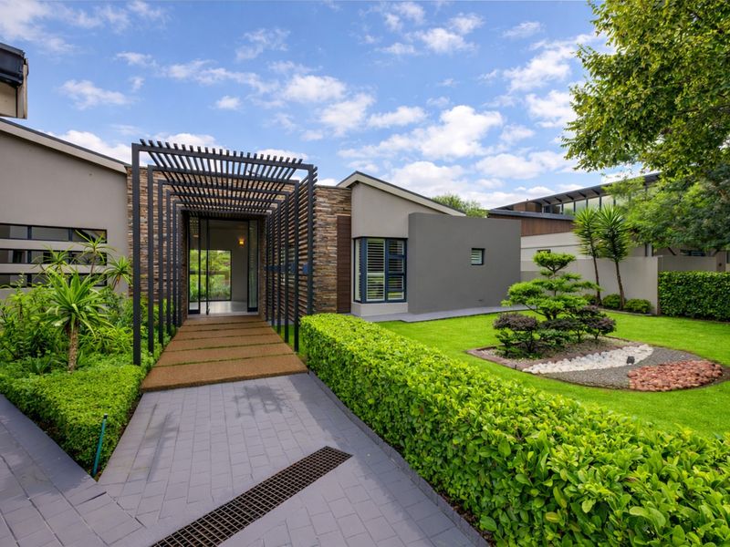 Modern front entrance featuring a striking pergola walkway, stone cladding accents, and a meticulously landscaped garden with paved pathways.