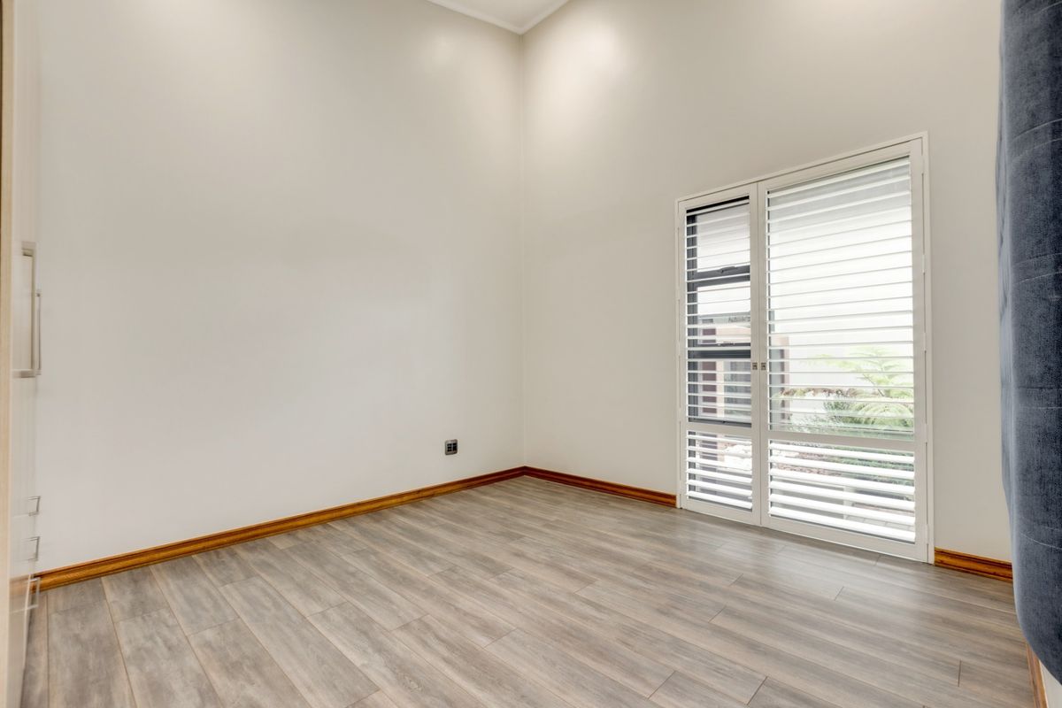 A bright, empty bedroom featuring modern laminate flooring, built-in cupboards, and a sliding glass door with integrated shutters providing access to the exterior.