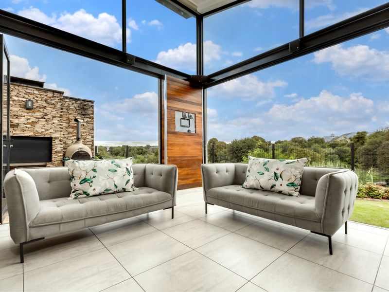 Modern enclosed patio featuring floor-to-ceiling glass walls, built-in braai, and pizza oven, offering seamless indoor-outdoor living with scenic views.