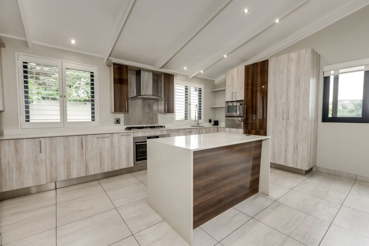 Modern kitchen featuring a central island, quartz countertops, built-in appliances, and high-quality cabinetry with a neutral tiled floor.