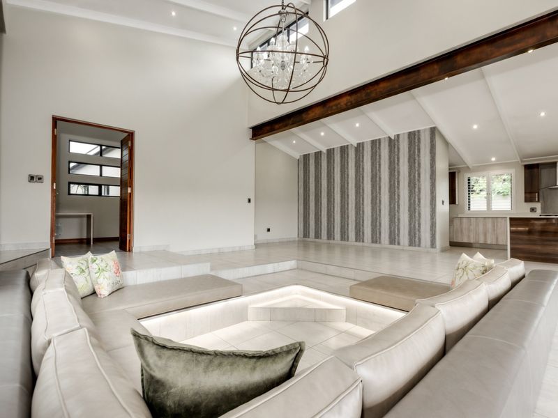 Spacious open-plan living area featuring a unique sunken conversation pit, vaulted ceilings with exposed beams, and a modern kitchen with integrated cabinetry.