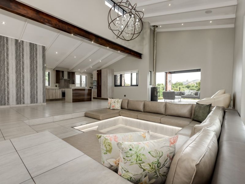 Spacious open-plan living area featuring a sunken lounge, vaulted ceilings with exposed beams, a modern kitchen, and seamless flow to an outdoor patio.