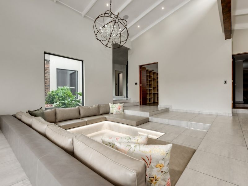 Spacious living room featuring a unique sunken conversation pit, vaulted ceilings with exposed beams, and large windows overlooking a private courtyard.