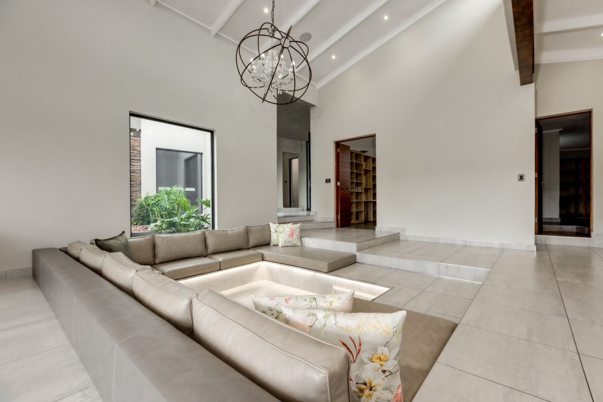 Spacious living room featuring a unique sunken conversation pit, vaulted ceilings with exposed beams, and large windows overlooking a private courtyard.
