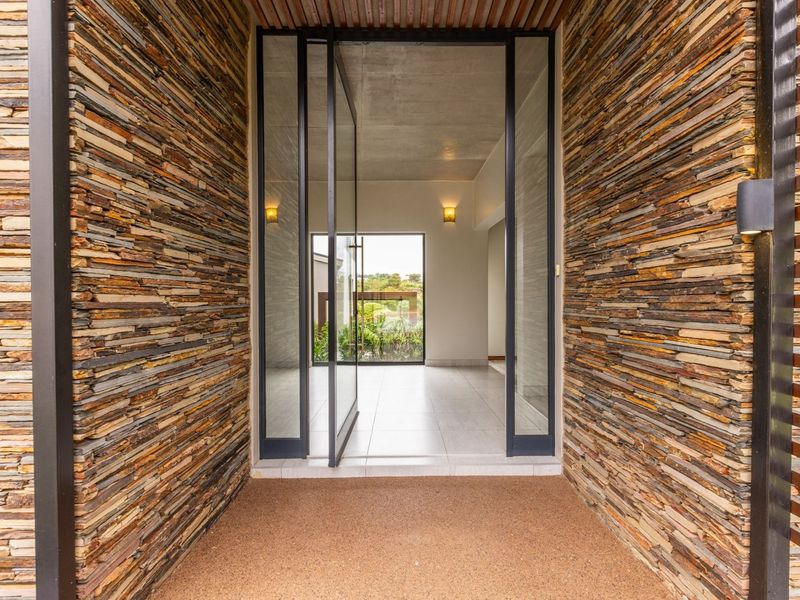 Modern entrance featuring striking stacked stone wall cladding, a large glass pivot door, and clean tiled flooring leading into the home.