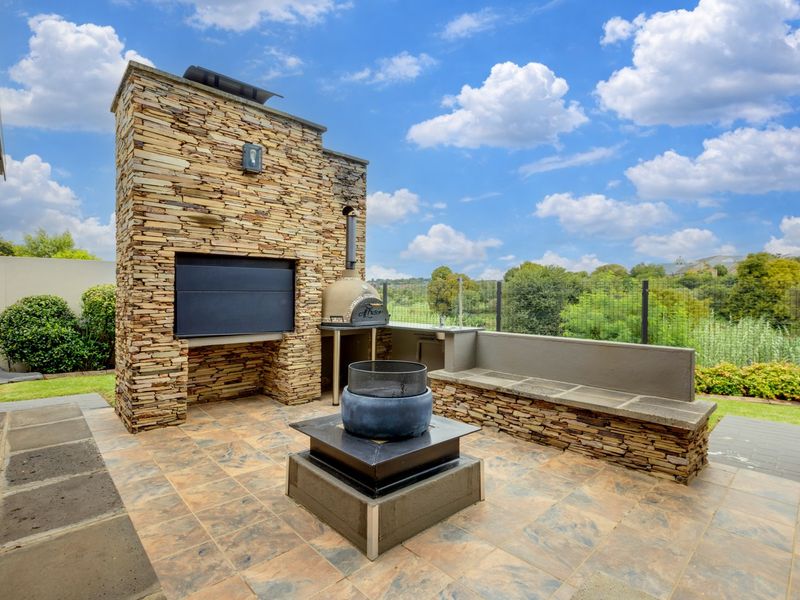 Outdoor patio area featuring a stone-clad fireplace, built-in pizza oven, and integrated stone bench seating, overlooking a landscaped garden.