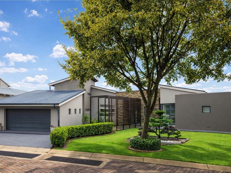 Modern front elevation featuring a metal roof, stone cladding accents, a timber slat screen, and a well-maintained landscaped garden with a paved driveway.
