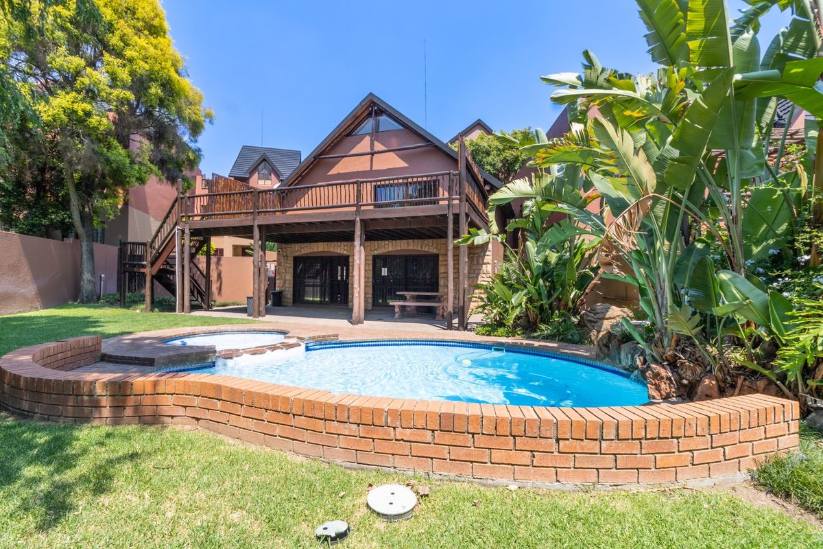 Rear view of the property featuring a swimming pool with brick coping, a raised wooden deck, and an external staircase leading to the upper level.