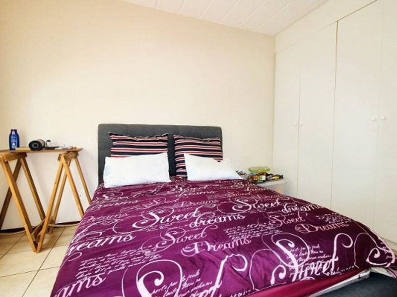 A functional bedroom featuring neutral walls, tiled flooring, and ample built-in cupboard storage space.