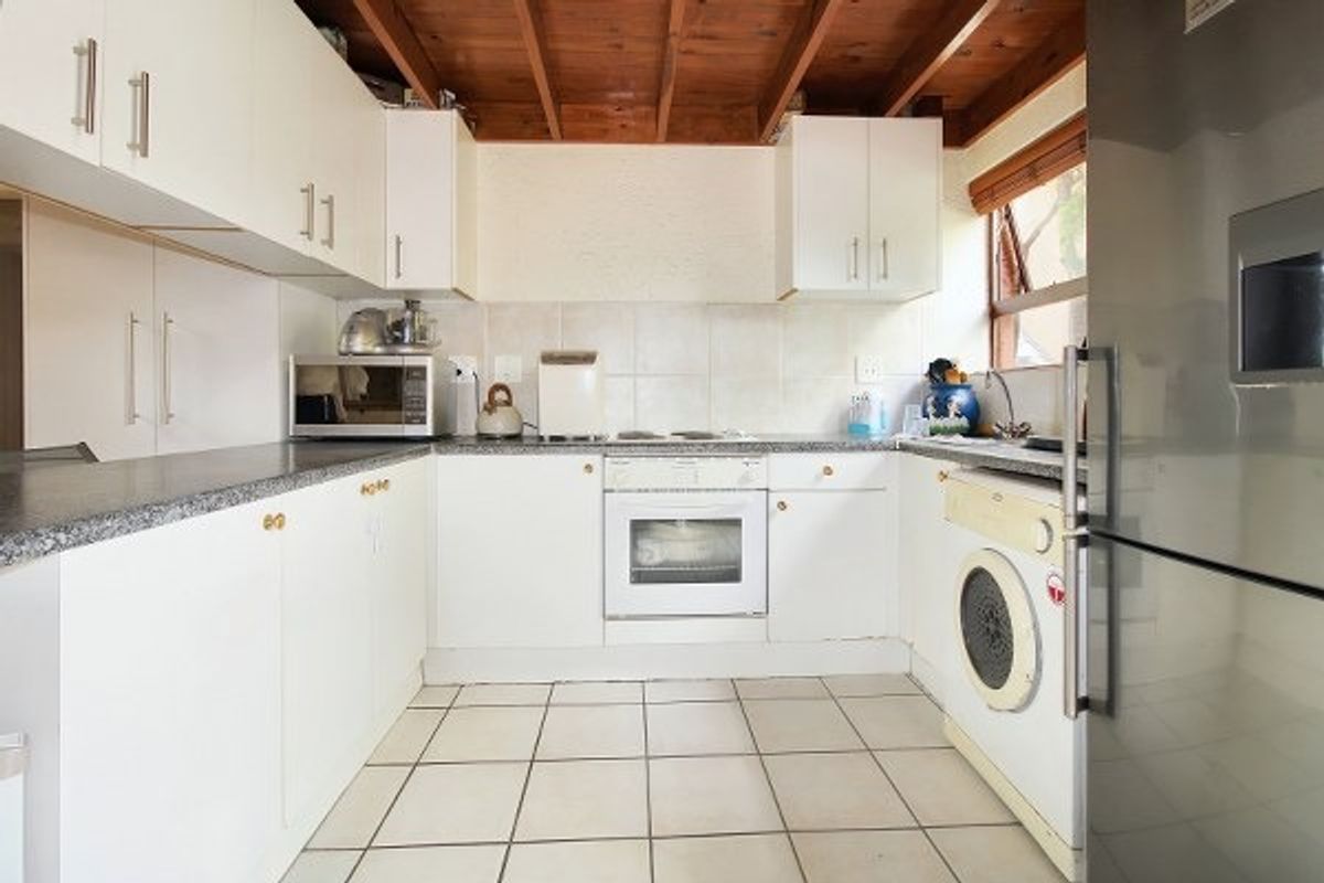 Functional kitchen featuring white cabinetry, laminate countertops, tiled backsplash, built-in oven, and exposed timber ceiling beams with integrated laundry plumbing.