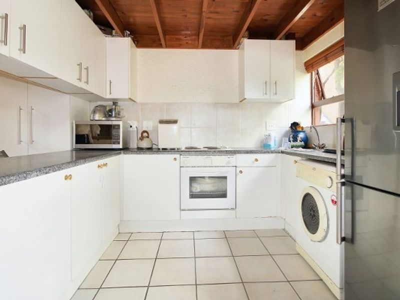 Functional kitchen featuring white cabinetry, laminate countertops, tiled backsplash, built-in oven, and exposed timber ceiling beams with integrated laundry plumbing.