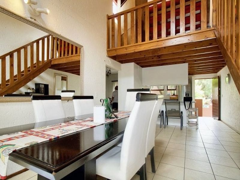Open plan living and dining area featuring a wooden staircase leading to a mezzanine level, tiled flooring, and a large wall mirror.