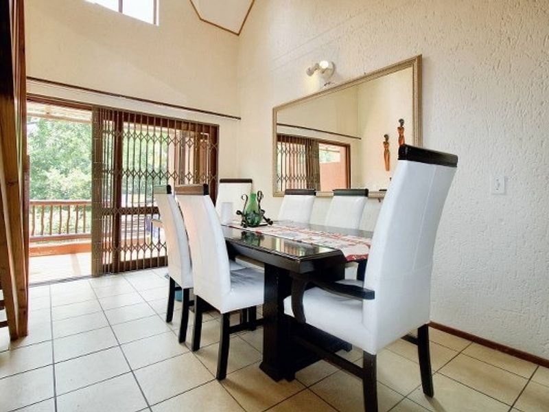 Dining area featuring tiled flooring, vaulted ceilings, and a sliding glass door with security gate leading to an outdoor balcony.
