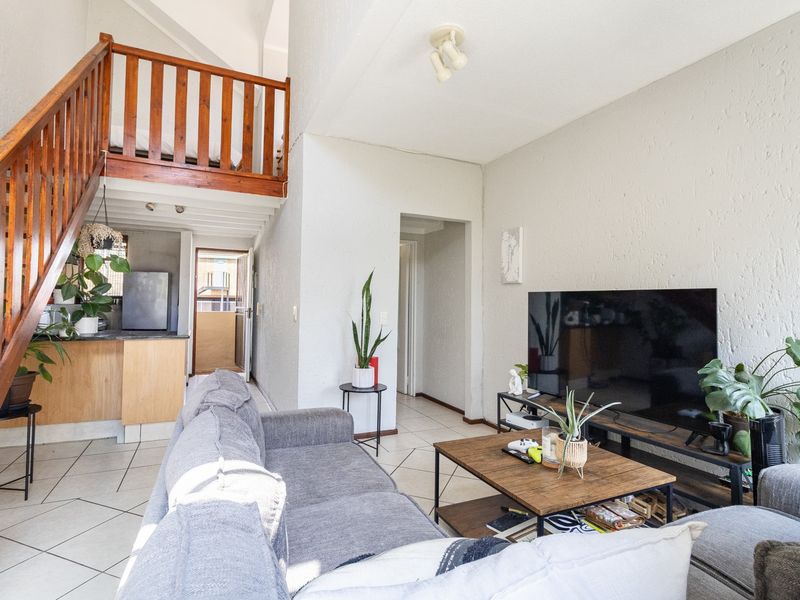 Open plan living area featuring a wooden staircase leading to a mezzanine level, tiled flooring, and textured walls with an adjacent kitchen space.