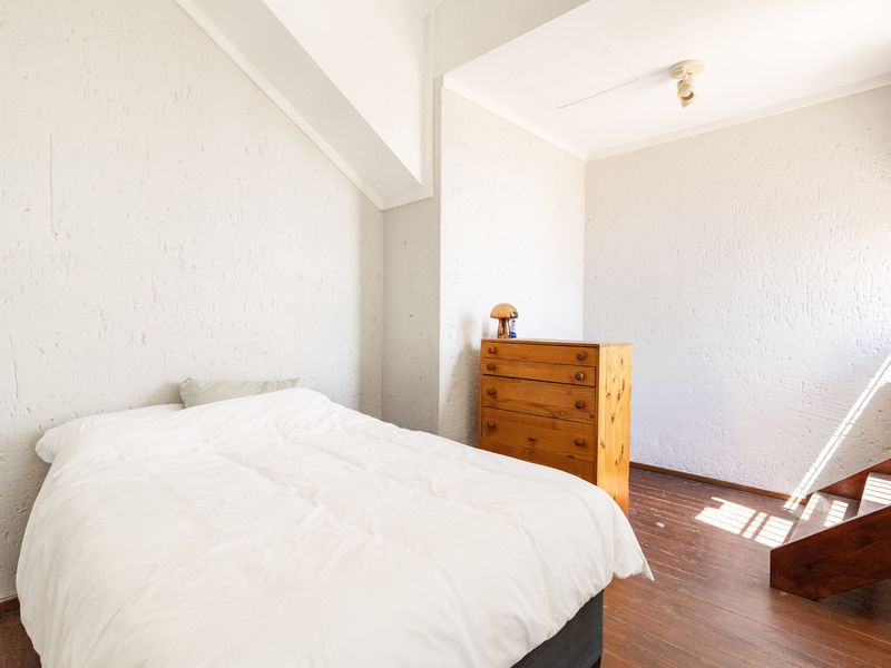 A bedroom featuring textured walls, sloped ceilings, and hardwood flooring, offering a functional space with potential for modern updates.