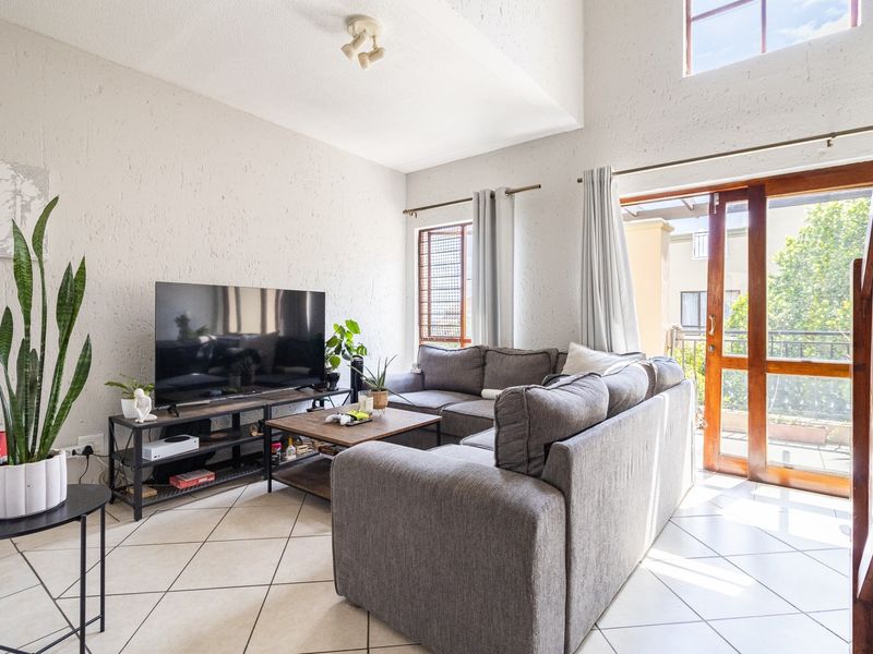 Spacious living room featuring high vaulted ceilings, tiled flooring, and a timber-framed glass door providing access to an outdoor balcony area.