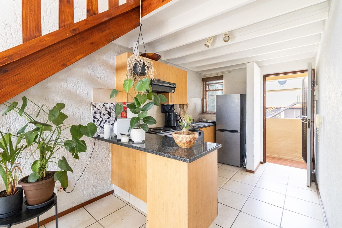 A functional kitchen featuring light wood cabinetry, granite countertops, and exposed ceiling beams, with direct access to an outdoor balcony area.
