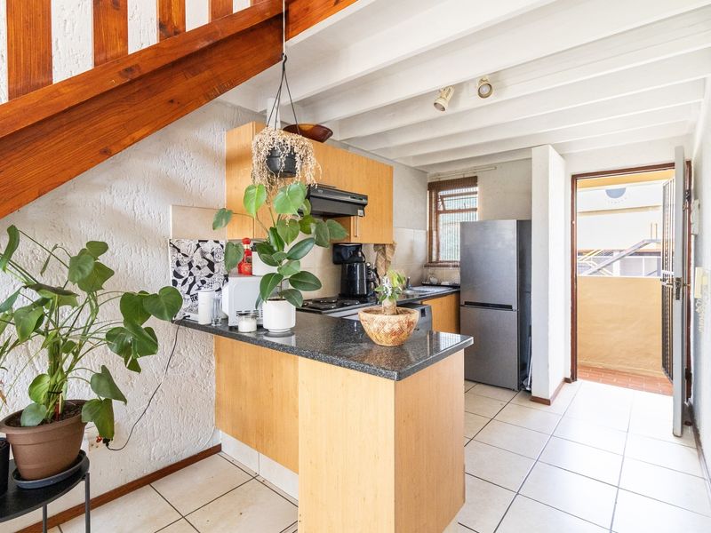 A functional kitchen featuring light wood cabinetry, granite countertops, and exposed ceiling beams, with direct access to an outdoor balcony area.
