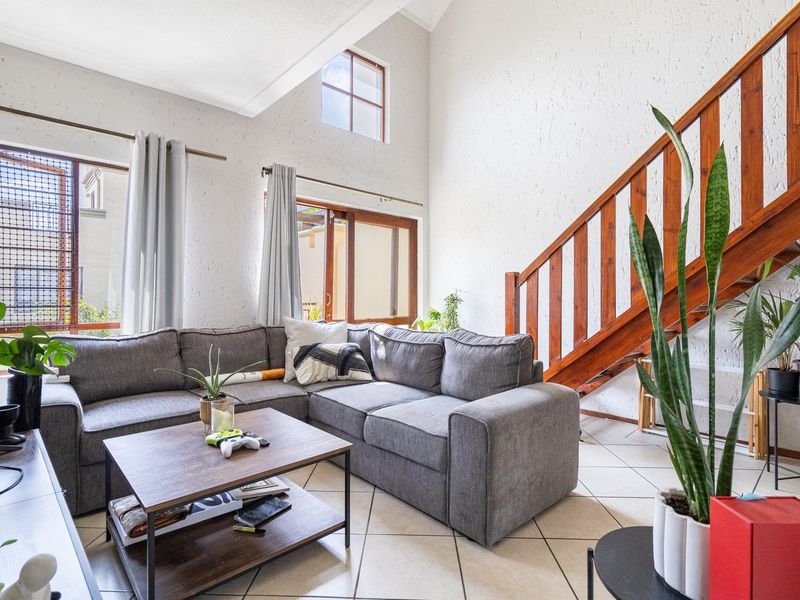 Spacious living room featuring high vaulted ceilings, a wooden staircase, and large windows that provide ample natural light.
