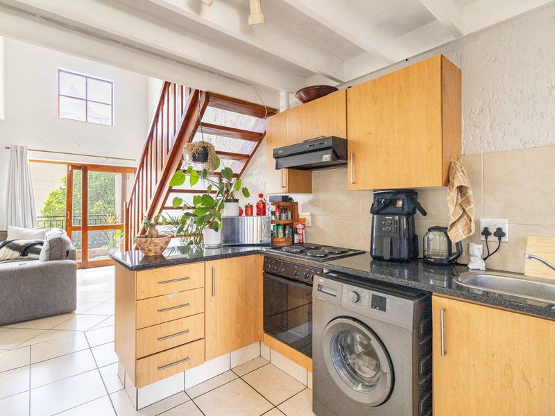 Open-plan kitchen featuring wooden cabinetry, granite countertops, and integrated appliances, seamlessly flowing into the living area with access to a balcony via sliding doors.