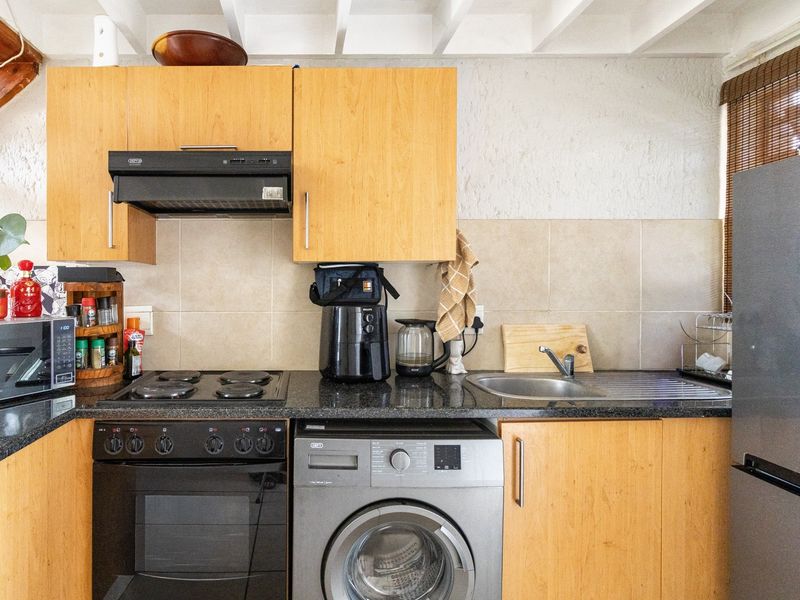 A functional kitchen featuring light wood cabinetry, granite countertops, a tiled backsplash, and integrated appliances including an oven, hob, and extractor fan.