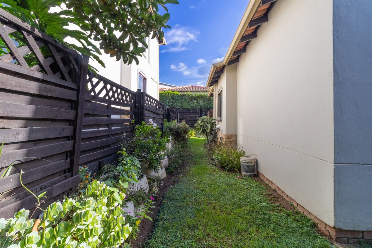 A narrow side garden path featuring a well-maintained lawn, landscaped garden beds, and timber lattice fencing along the property boundary.