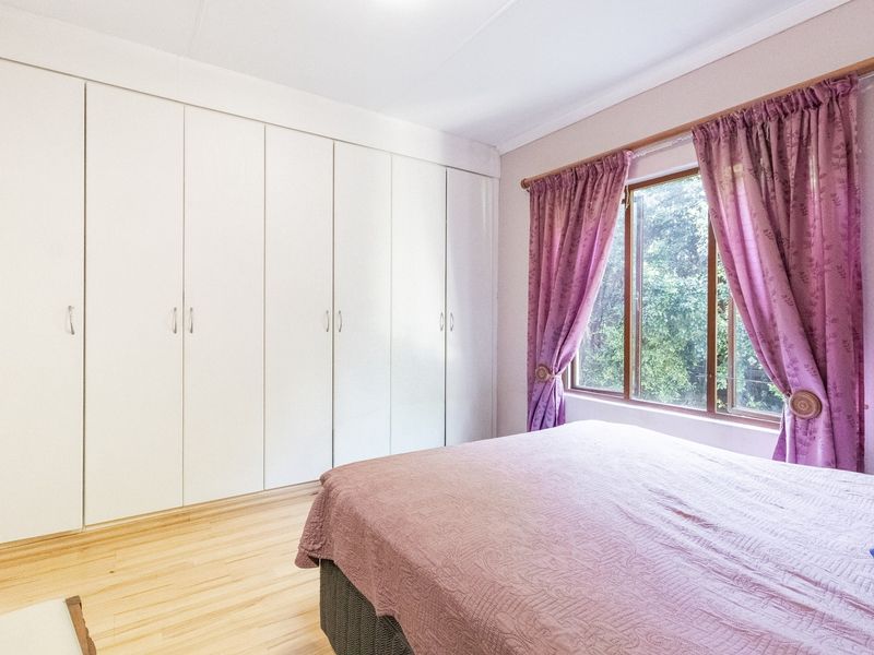 A bedroom featuring extensive floor-to-ceiling built-in cupboards and light-toned laminate flooring, offering ample storage space and natural light.