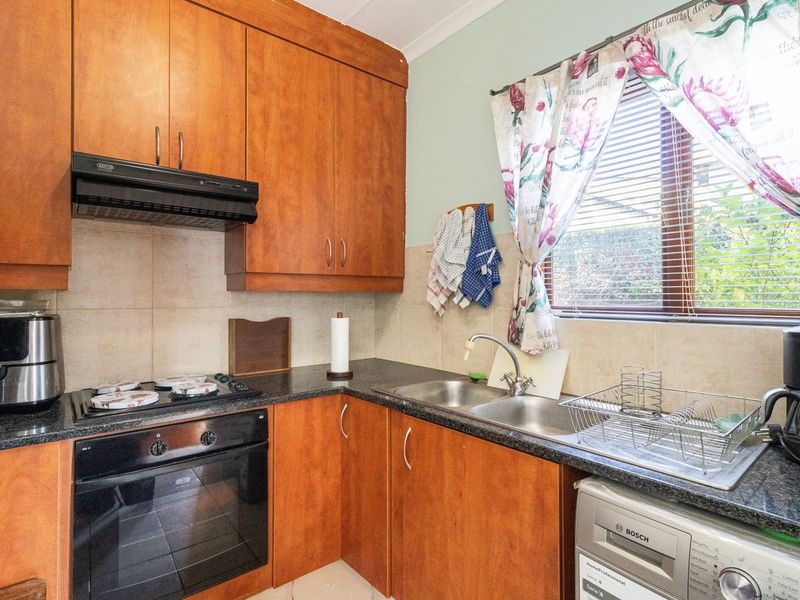 A functional kitchen featuring wood-finish cabinetry, granite countertops, a built-in oven with gas hob, and a stainless steel double sink.