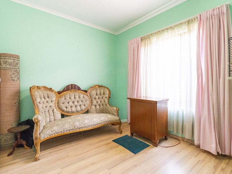 A living room featuring light-toned laminate flooring, coved ceilings, and a large window with curtains.