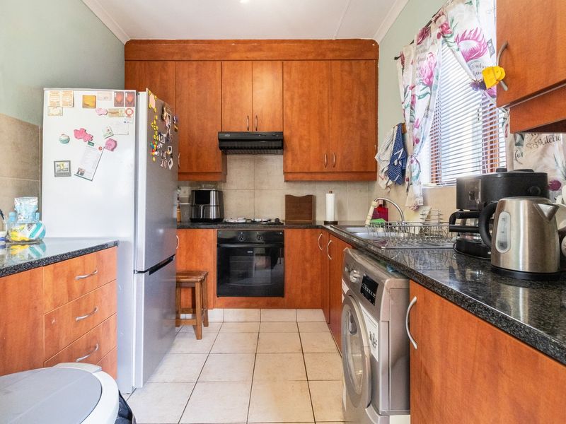 A functional kitchen featuring wood-finish cabinetry, granite countertops, built-in oven, hob, extractor fan, and tiled flooring with integrated laundry plumbing.