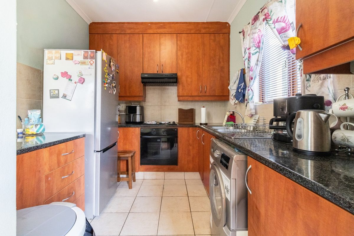 A functional kitchen featuring wood-finish cabinetry, granite countertops, built-in oven, hob, extractor fan, and tiled flooring with integrated laundry plumbing.