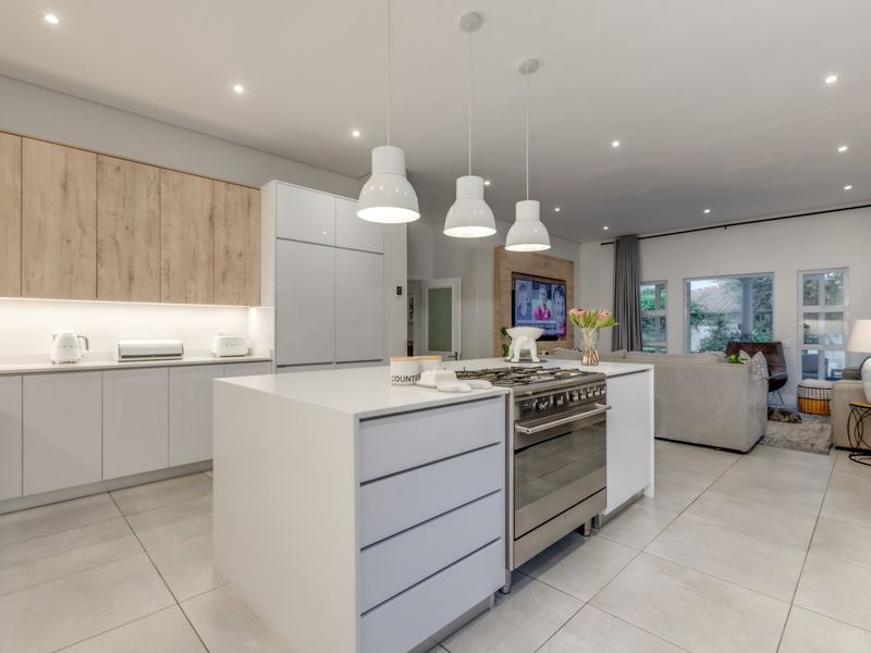 Modern open-plan kitchen and living area featuring a central island with gas stove, sleek cabinetry, and contemporary recessed lighting throughout.
