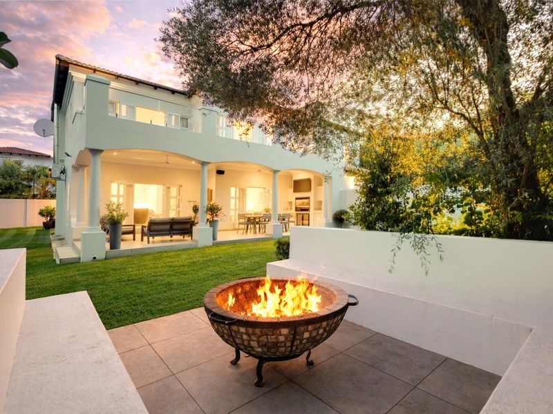A beautifully landscaped rear garden featuring a covered patio with built-in braai, tiled flooring, and a dedicated fire pit area.