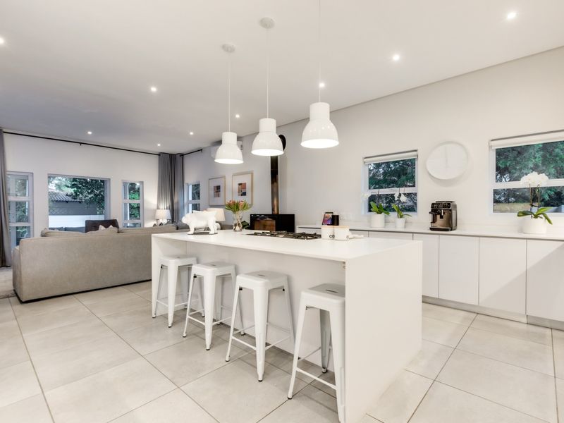 Modern open-plan kitchen and living area featuring a central island, gas hob, sleek cabinetry, and contemporary pendant lighting with neutral tiled flooring throughout.