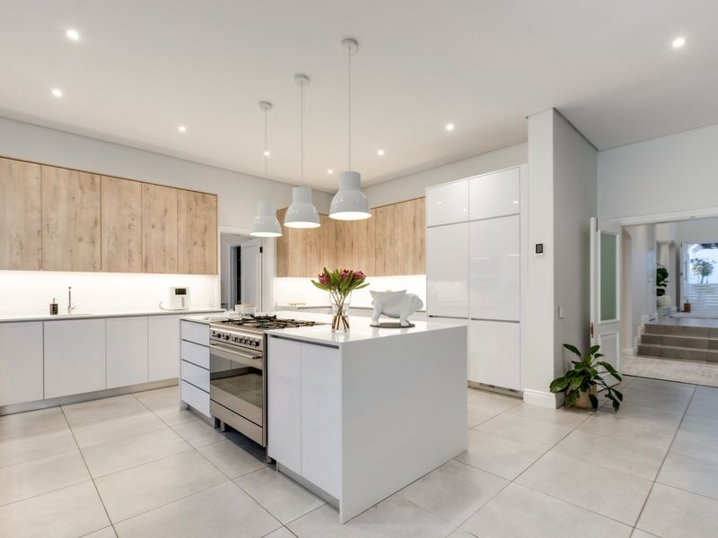 Modern kitchen featuring a central island with gas cooktop, integrated cabinetry, sleek white finishes, and warm wood-tone upper cabinets with under-cabinet lighting.
