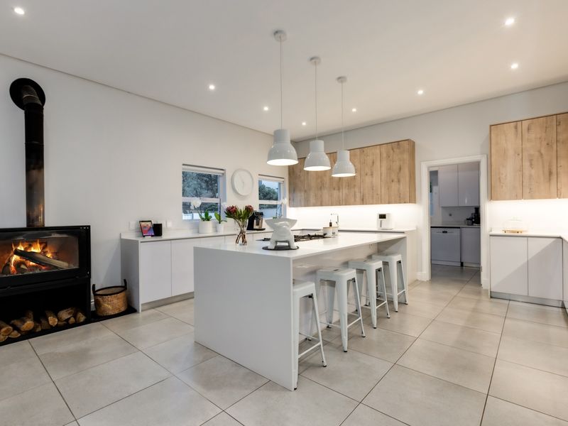 Modern open-plan kitchen featuring a central island, sleek cabinetry, stone countertops, and a built-in fireplace, complemented by recessed and pendant lighting.