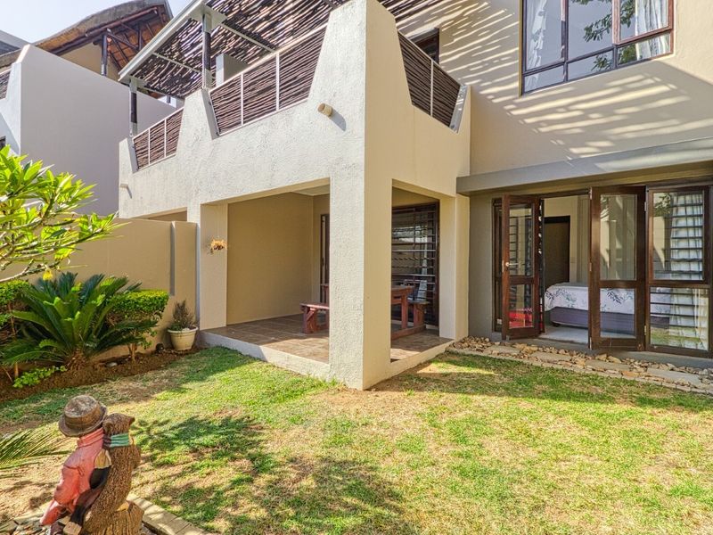 A well-maintained rear exterior view featuring a covered patio, an upper-level balcony with timber detailing, and a private landscaped garden area.