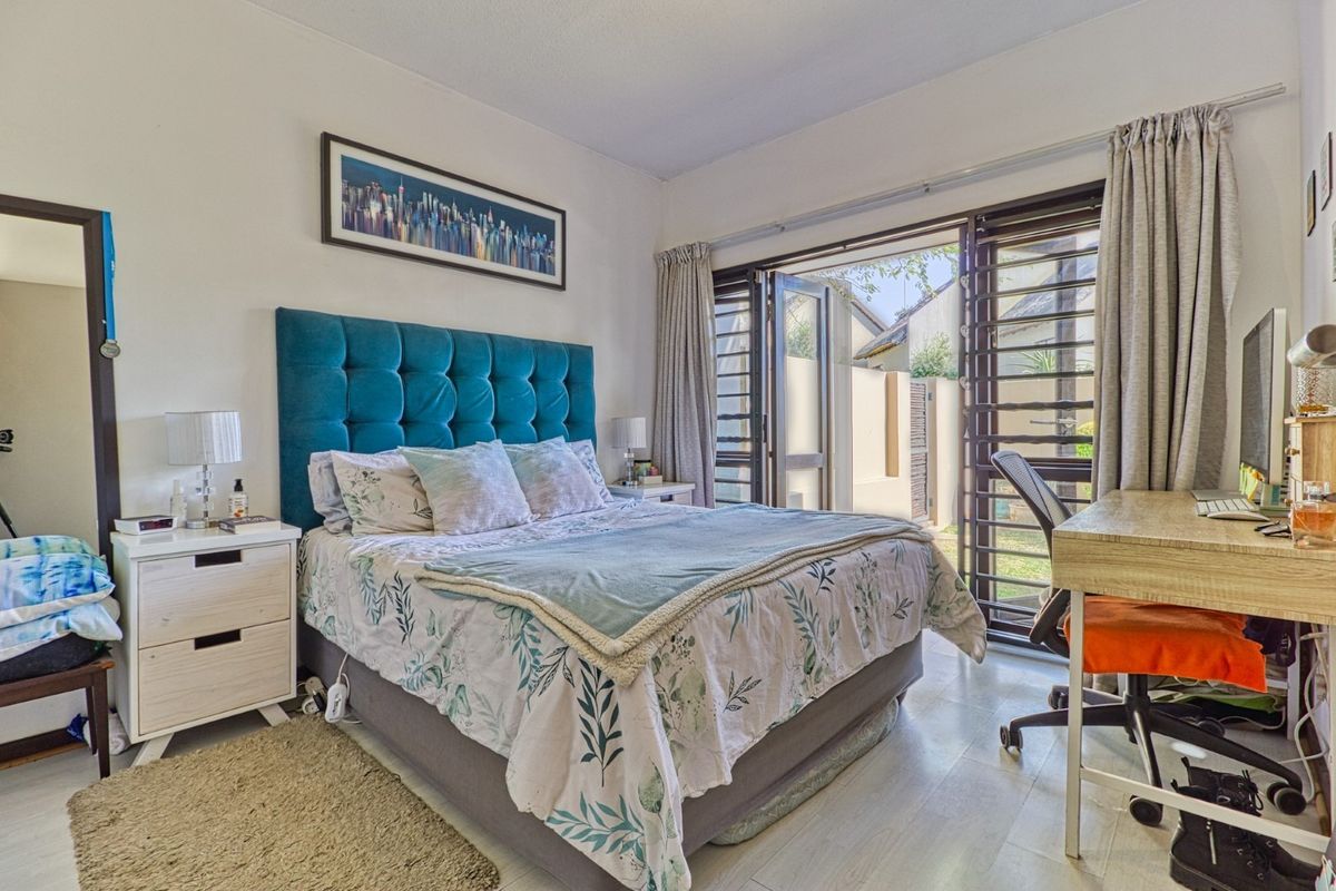 A well-lit bedroom featuring laminate flooring and louvered security shutters, with direct access to an outdoor area through a sliding glass door.