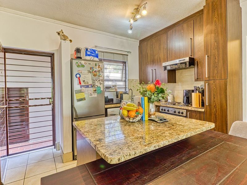 Compact kitchen featuring dark wood cabinetry, granite countertops, and integrated appliances, with direct access to an exterior security gate.