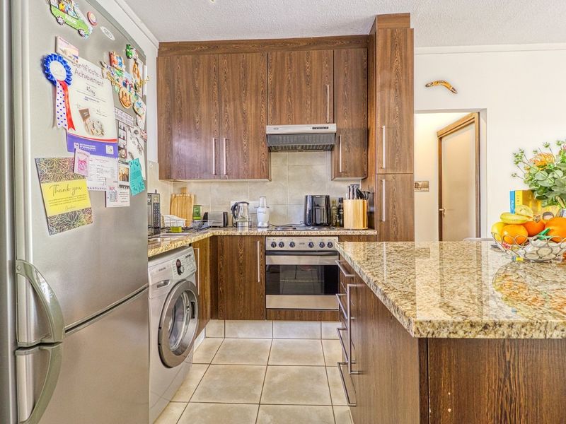 Compact kitchen featuring dark wood-look cabinetry, granite countertops, tiled flooring, and built-in appliances including an oven and integrated washing machine.
