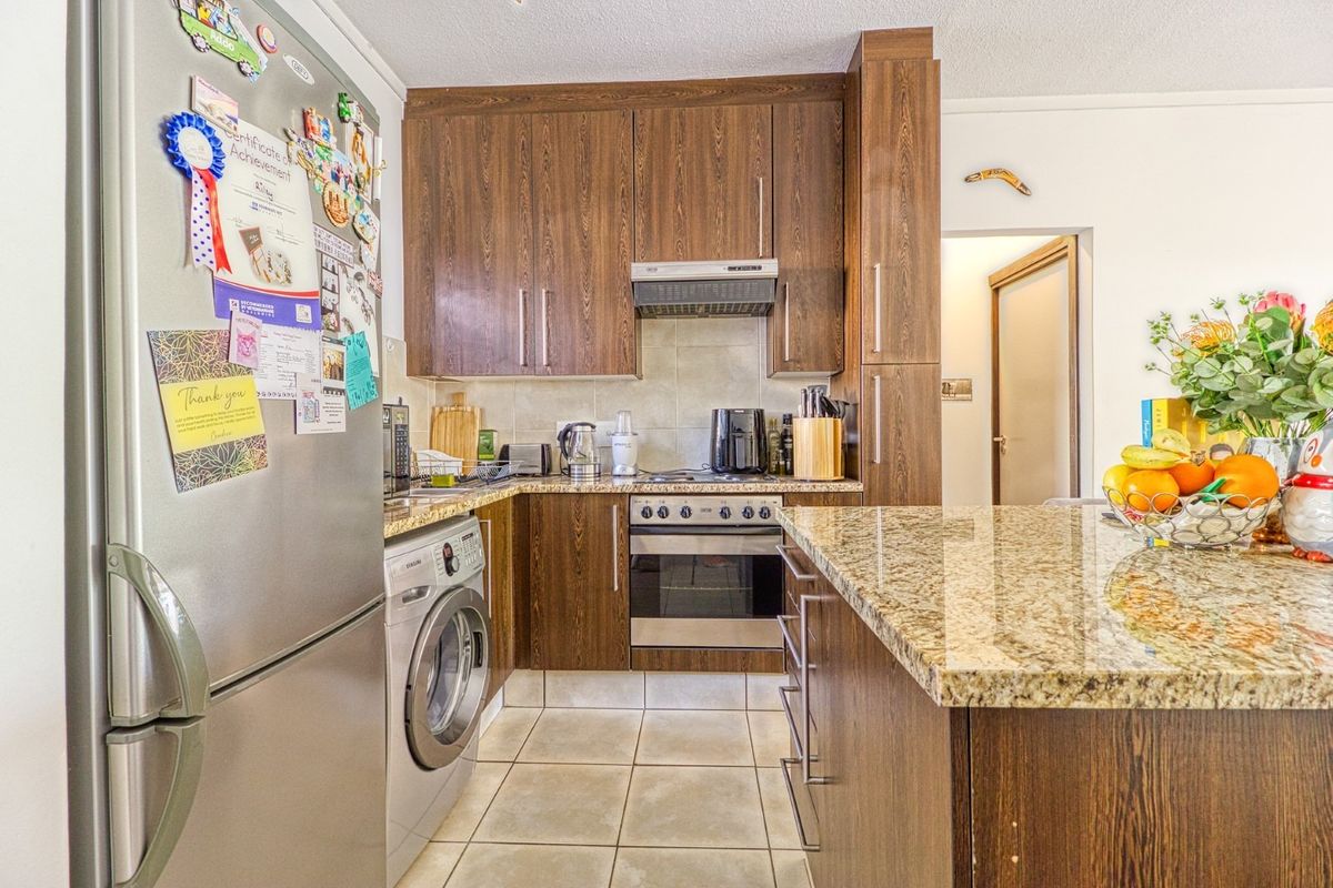 Compact kitchen featuring dark wood-look cabinetry, granite countertops, tiled flooring, and built-in appliances including an oven and integrated washing machine.