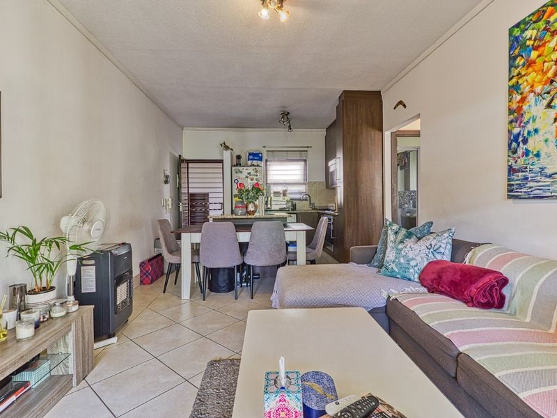 Open-plan living and dining area featuring tiled flooring, flowing into a functional kitchen with built-in cabinetry and appliances.