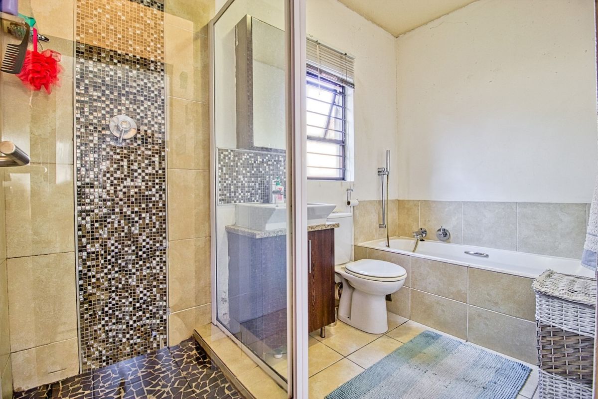 A functional bathroom featuring a separate shower enclosure with mosaic tiling, a bathtub, a vanity unit with a vessel sink, and a toilet.